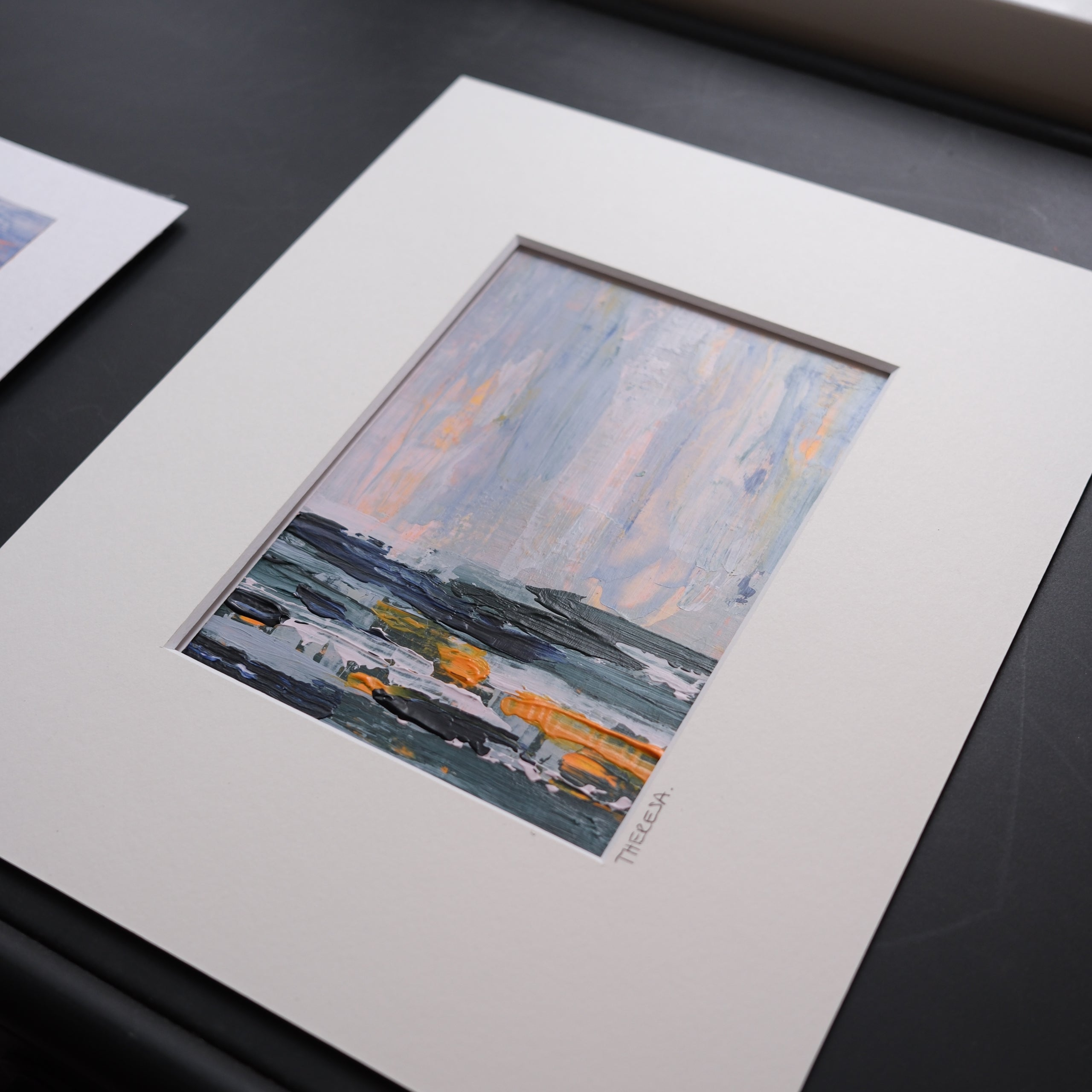 Framed artwork of a boat on water with a white mat on a dark surface